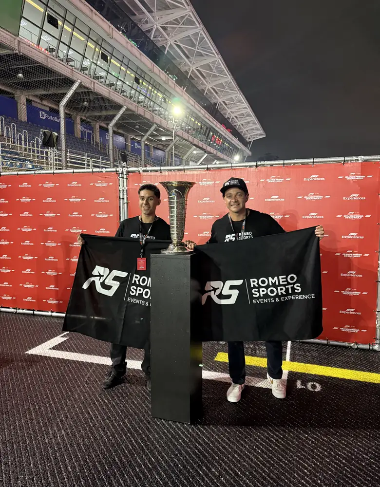Dos integrantes del equipo de Romeo Sports con banderas junto al trofeo del GP de São Paulo, en Interlagos